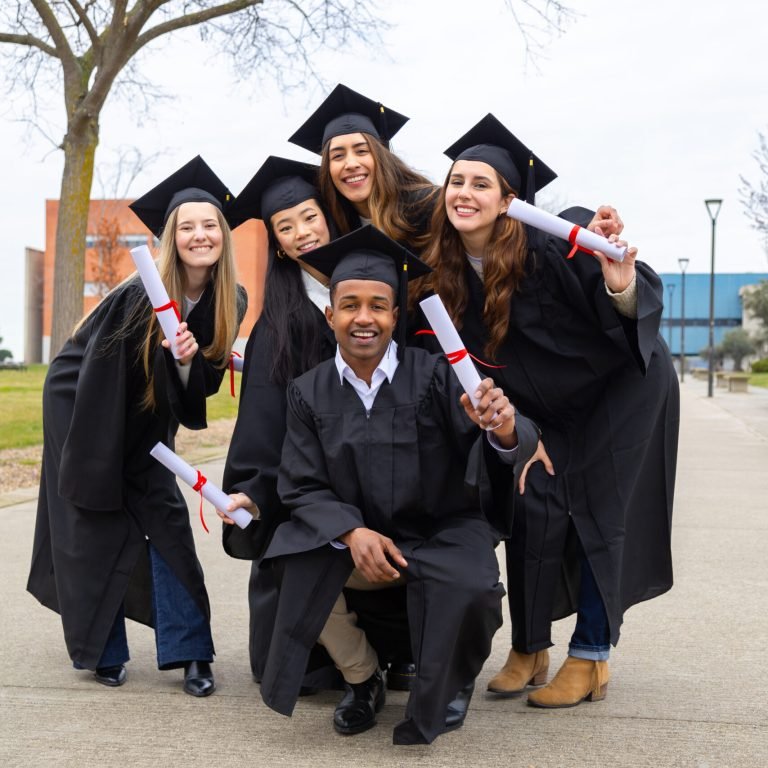Cheerful multiethnic graduates in academic gowns proudly displaying diplomas while celebrating their achievements on the university campus